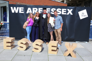 Eine Gruppe von Menschen, die lächeln und ein Zertifikat halten, vor einem Gebäude und einem Netz im Hintergrund.