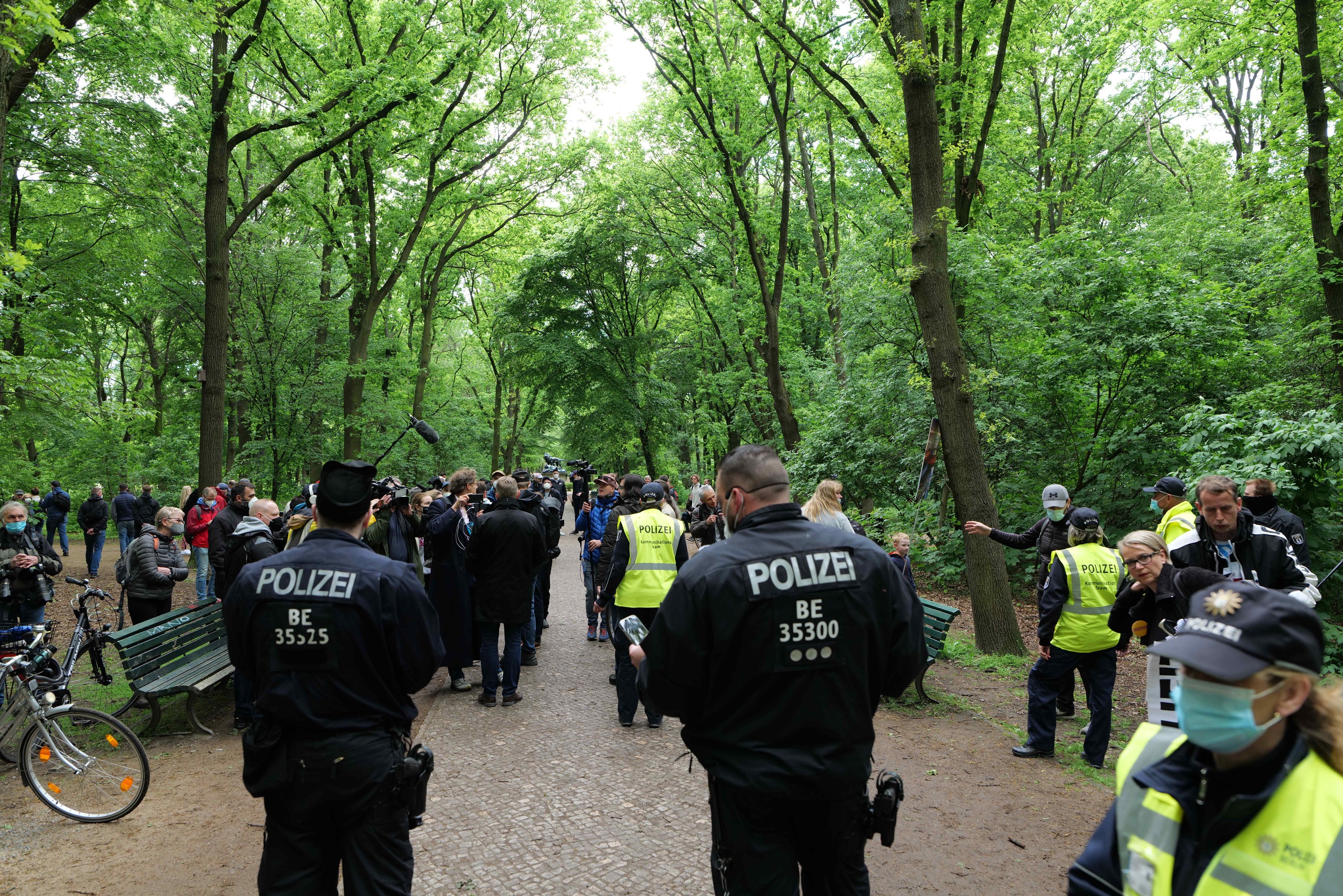Polizeibeamte vor einer Menge bei einem Outdoor-Event mit Fahrrädern und einer Bank im Vordergrund.