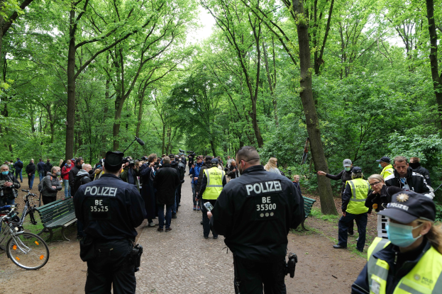 Polizeibeamte vor einer Menge bei einem Outdoor-Event mit Fahrrädern und einer Bank im Vordergrund.