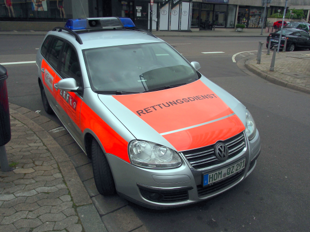 Polizeiauto am Straßenrand mit Müchel auf dem Gehweg links, Gebäude und Bäume im Hintergrund.