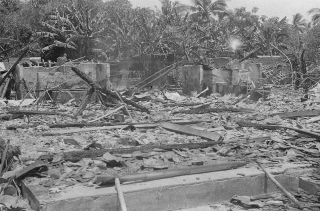 Ein Schwarz-Weiß-Foto eines zerstörten Gebäudes inmitten eines Waldes, mit Trümmern auf dem Boden und Bäumen im Hintergrund.