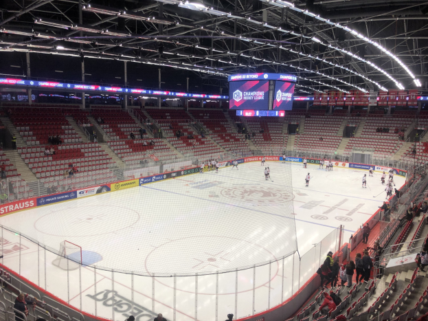 Hockey-Spiel in einer grossen Arena zwischen den St. Louis Blues und Detroit Red Wings, mit Zuschauern auf den Sitzen und Stehplätzen in der Nähe des Eises, umgeben von einem Zaun, einem Bildschirm, Metallrahmen, Deckenleuchten und einem Dach.