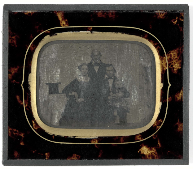 Schwarzes-Weiß-Foto eines Mannes in Anzug und Krawatte und einer Frau in unbekannter Kleidung, die vor einem Fernseher stehen, beide mit ernsten Gesichtern.