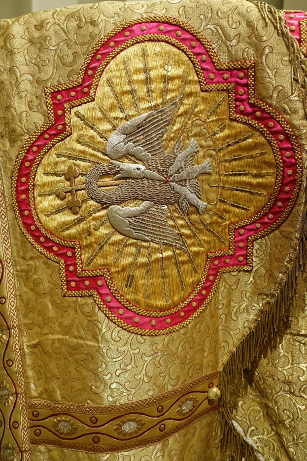 Nahaufnahme eines Priestergewandes mit aufwendiger goldener und roter Stickerei vor einer Wand im Hintergrund
