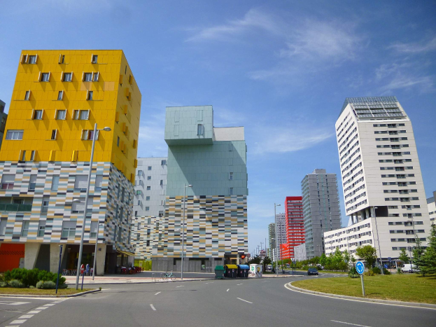 Eine Stadtstraße mit hohen Gebäuden im Hintergrund, Straßenlaternen, Verkehrspolizei, Motorfahrzeugen, Informationsanzeigen, Büschen, Bäumen und einem bewölkten Himmel, mit der einzigartigen Architektur der Universität Rotterdam.
