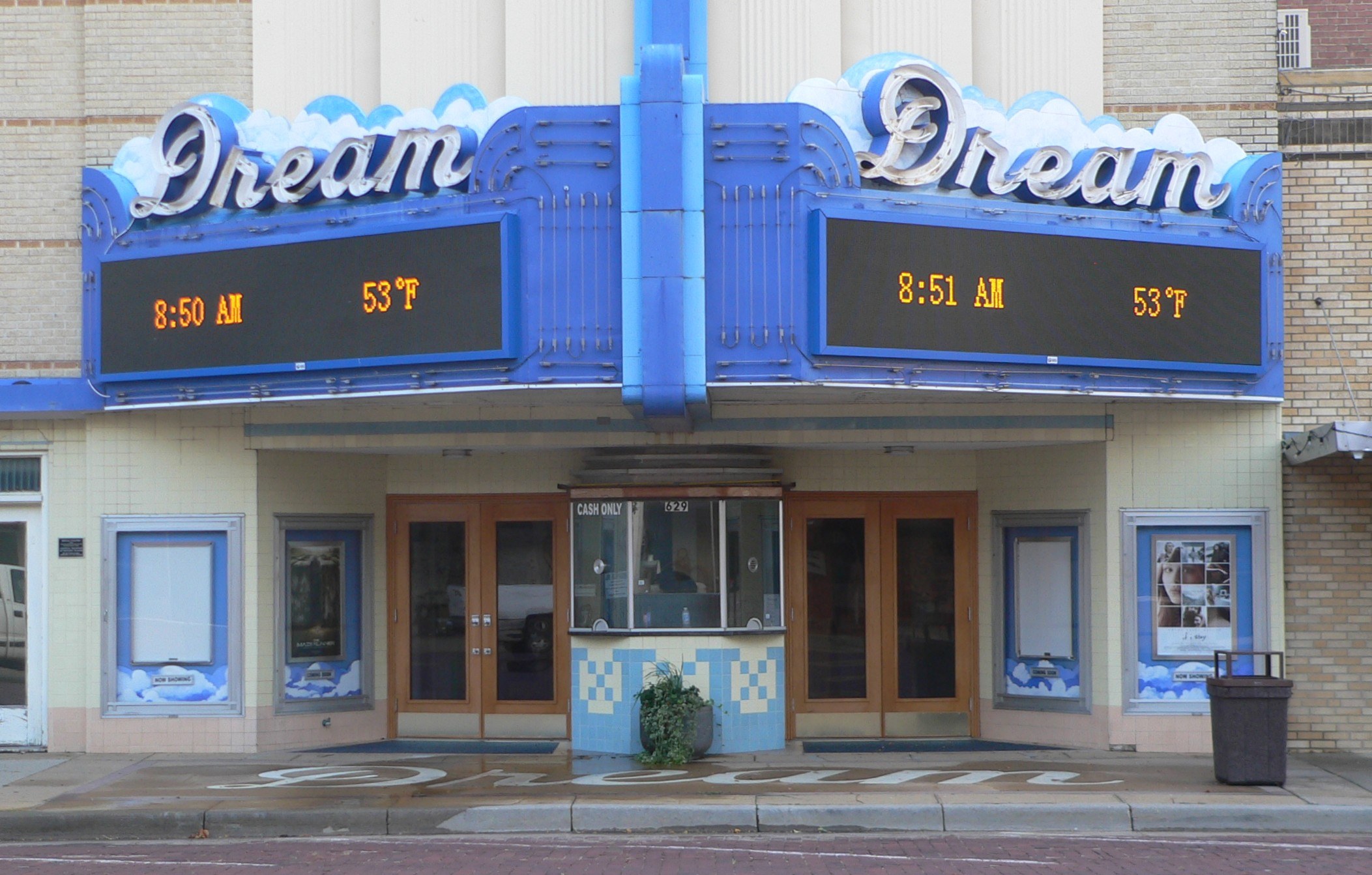 Außenansicht des Dream Theaters in St. Louis, Missouri, mit Glastüren und -fenstern, einem Namen auf einem Schild, einem Mülleimer, einem Topf mit einer Pflanze und einer Straße im Vordergrund.
