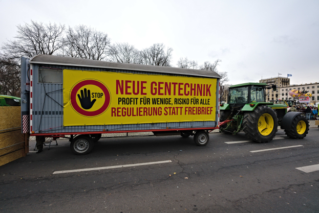 Ein Lastwagen mit einer Aufschrift auf der Rückseite, der auf einer Straße fährt, umgeben von Menschen, Bäumen, Gebäuden und einem klaren blauen Himmel, wahrscheinlich Teil einer Demonstration in Deutschland.