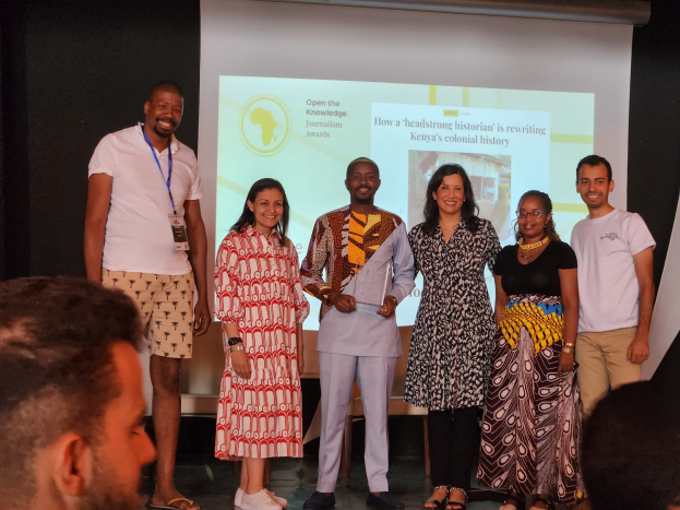 Gruppe von Menschen auf einer Bühne, die für ein Foto lächeln, mit einem Publikum, das darunter sitzt, und einem Bildschirm im Hintergrund, der "Open the Knowledge Journalism Awards 2019" anzeigt.