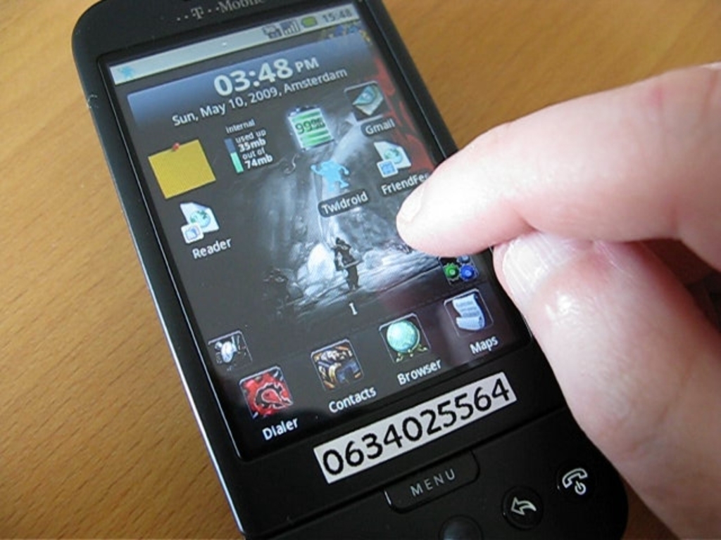 Eine Person nutzt ein Mobiltelefon auf einem Tisch, mit mehreren Apps auf dem Bildschirm und einem Stück Papier mit einer Zahl daran befestigt.