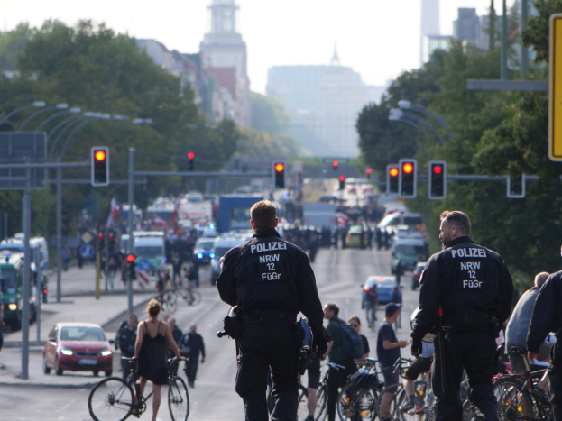 Polizeibeamte fahren mit Fahrrädern eine straßenlange Allee mit Gebäuden und einem klaren Himmel im Hintergrund entlang.
