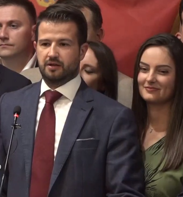 Ein Mann im Anzug spricht an einem Podium mit einem Mikrofon zu einer Menge hinter einem Banner, wahrscheinlich über ein Regierungssozialmedienverbot.