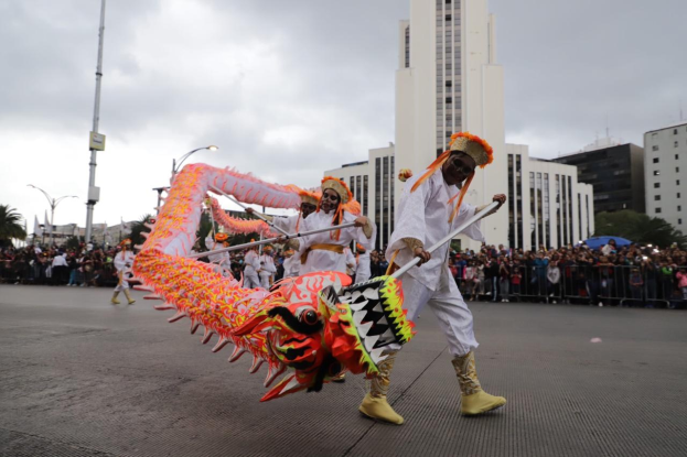 Eine Gruppe von Menschen in Kostümen führt einen Drachen Tanz mit Stöcken vor einem Publikum während der chinesischen Neujahrsfeier in Brisbane durch, mit Gebäuden, Bäumen und Laternenmasten im Hintergrund.