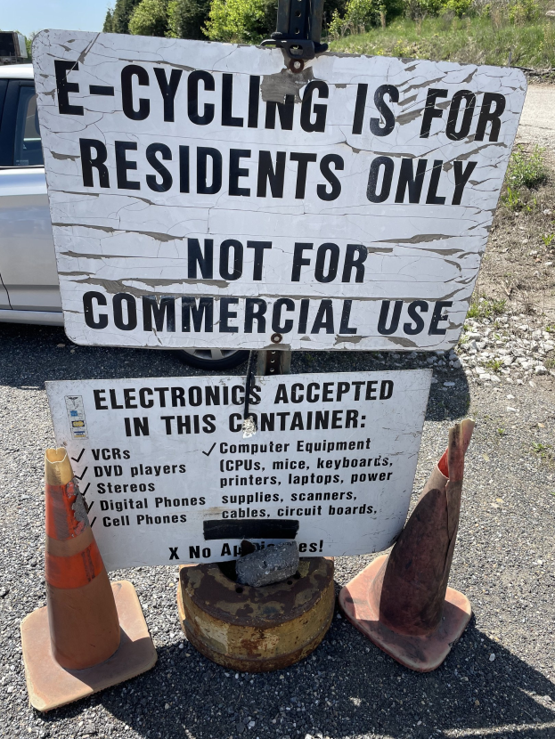 Schild mit Aufschrift "e-Bike nur für Anwohner" neben einer Straße mit Verkehrskegeln, einem Fahrzeug, Bäumen und einem klaren blauen Himmel im Hintergrund.