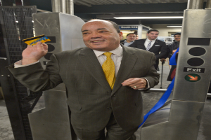 Eine Person hält eine Karte in der Nähe eines Ausgangsschilds mit einer blauen Schleife und einem Grill auf der linken Seite sowie mehreren Personen im Hintergrund.