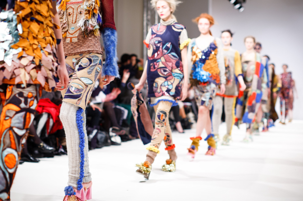 Eine Gruppe Von Frauen, Die Eine Laufsteg In London Fashion Week Heruntergehen, Mit Einer Zuschauerschaft Im Hintergrund Unter Helllem Licht.