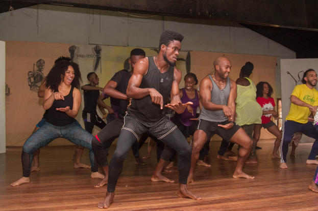 Eine Gruppe von Menschen tanzt in einem Raum mit Wandgemälden und einer Decke, wahrscheinlich an einer Choreographie-Klasse an der Universität Chicago teilnehmend.