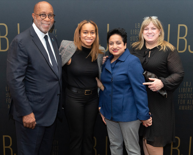 Eine Gruppe von vier Menschen auf einem roten Teppich, die lächeln und für ein Foto posieren, mit einer Tafel im Hintergrund, auf der "Liberty Justice for All Awards" steht.
