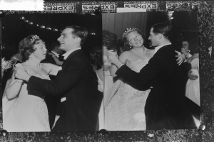 Ein Schwarz-Weiß-Foto eines Brautpaares in Weiß und Schwarz, das zusammen tanzt und von einer Gruppe Menschen umgeben ist, die beide lächeln und Spaß haben.