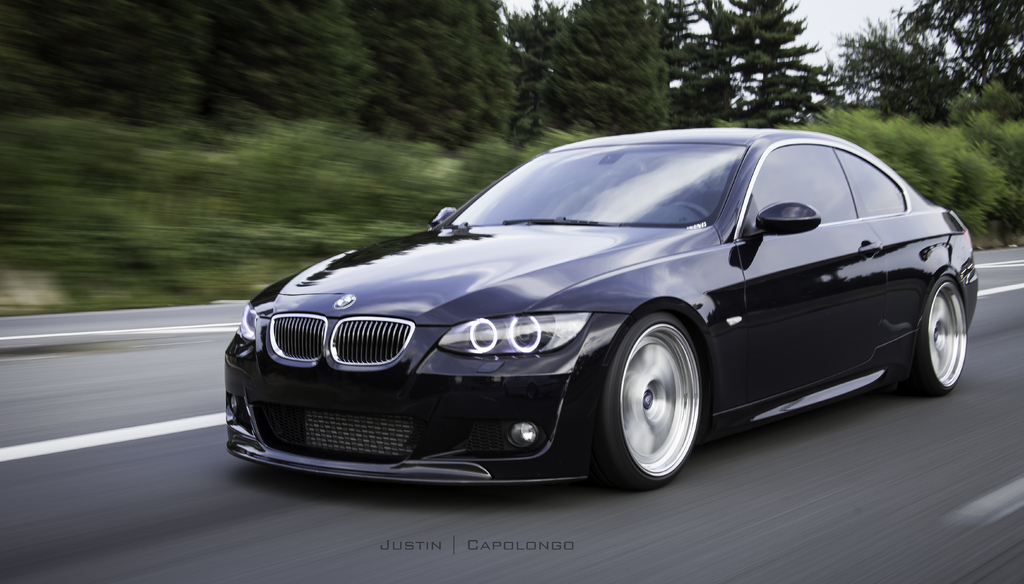 Ein schwarzer BMW f√§hrt auf einer Stra√Ÿe mit B√§umen im Hintergrund.