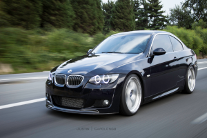 Ein schwarzer BMW f√§hrt auf einer Stra√Ÿe mit B√§umen im Hintergrund.