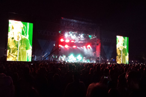 Eine Konzertszene mit einer Menge unten und großen Bildschirm links und kleiner rechts.