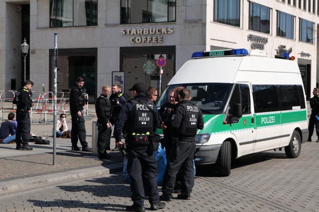 Gruppe von Polizisten vor einem Starbucks-Café mit einem Van auf der rechten Seite und Menschen auf der linken Seite, Hintergrund enthält ein Gebäude mit Fenstern, ein Schild, eine Straßenlaterne und eine Umzäunung.