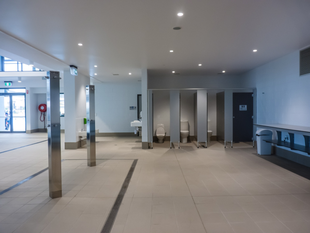 Großeßöffentliche Toilette mit mehreren Toiletten, Säulen, einem Mülleimer, einer Tür, einem Schilder, einem Feuerlöscher und Deckenleuchten.