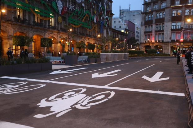 Stadtstraße mit einem ausgewiesenen Fahrradweg, umgeben von Gebäuden, Straßenmöbeln, Fußgängern und Grünflächen unter einem klaren blauen Himmel.