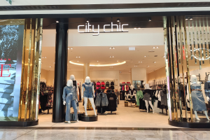 Ein stylischer Mode-Laden in einem Einkaufszentrum mit Schaufensterpuppen in der neuesten Mode, Kleidung an Bügeln, einer Säule, einem Schild und einer Fliesenboden.