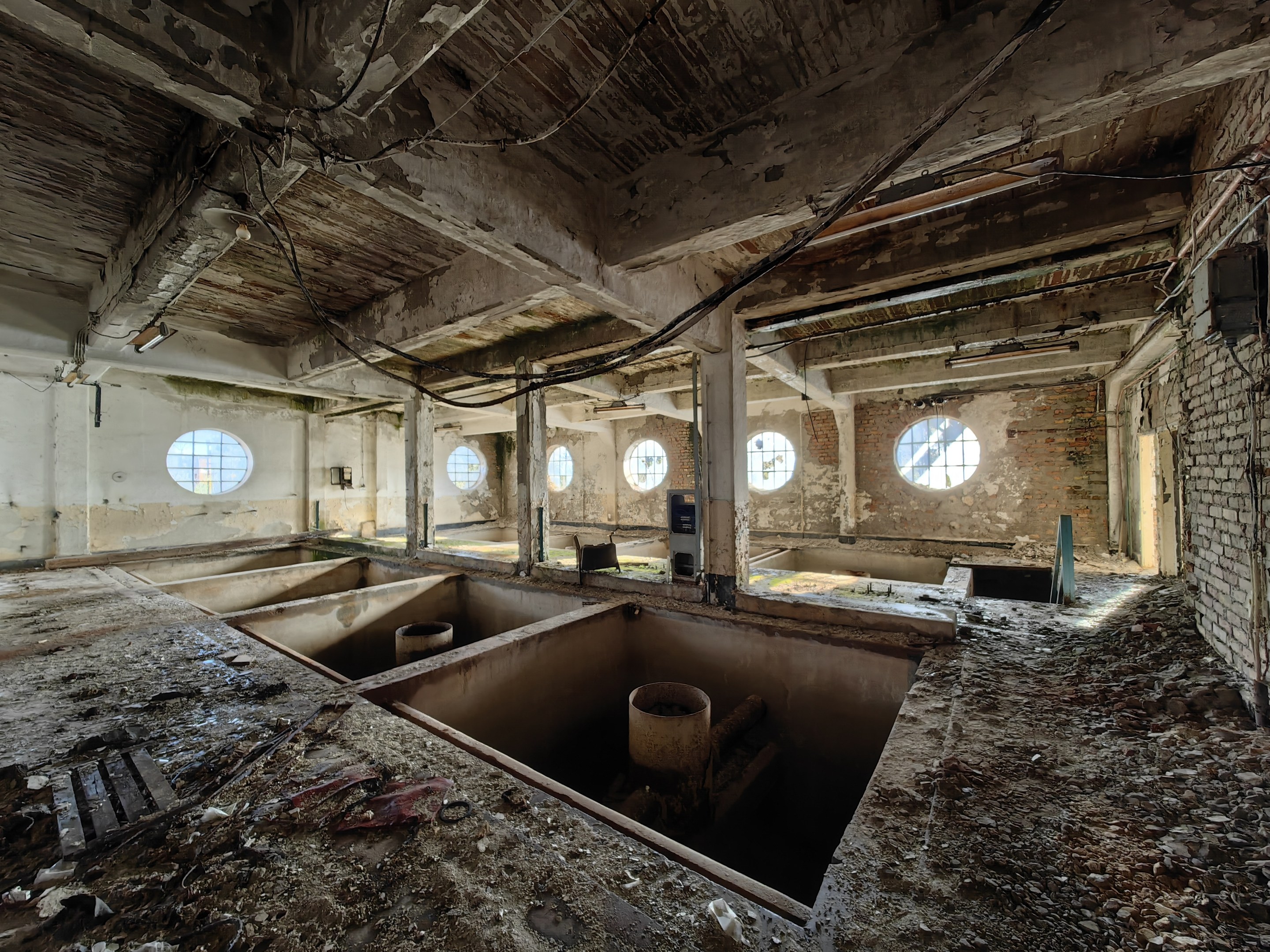 Verlassener Gebäuderaum im Sperrgebiet von Tschernobyl mit verstreuten Trümmern, freiliegenden Wänden, Decke und zahlreichen Fenstern und Säulen.