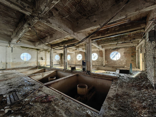 Verlassener Gebäuderaum im Sperrgebiet von Tschernobyl mit verstreuten Trümmern, freiliegenden Wänden, Decke und zahlreichen Fenstern und Säulen.