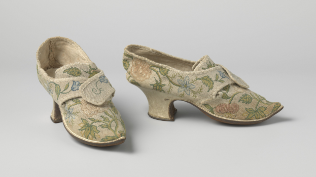 Frauen-Sandalen mit niedriger Absatzhöhe und gerundeter Spitze, verziert mit floraler Stickerei in Rosa, Lila und Grün, auf einer weißen Oberfläche präsentiert.