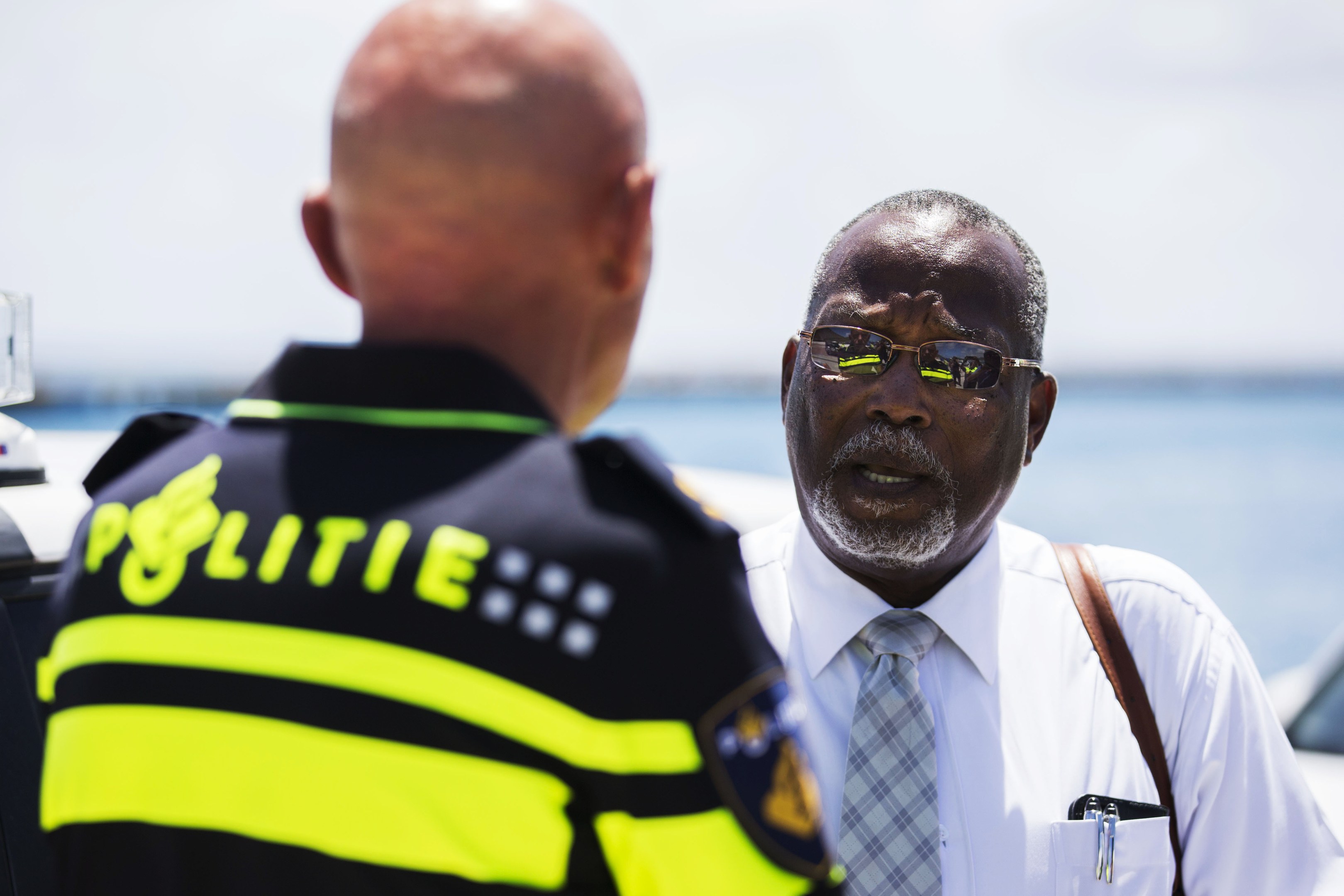 Zwei Männer im Gespräch, einer in einem weißen Hemd und Krawatte, der andere in einer schwarzen und gelben Polizeiuniform, mit einem unscharfen Hintergrund.