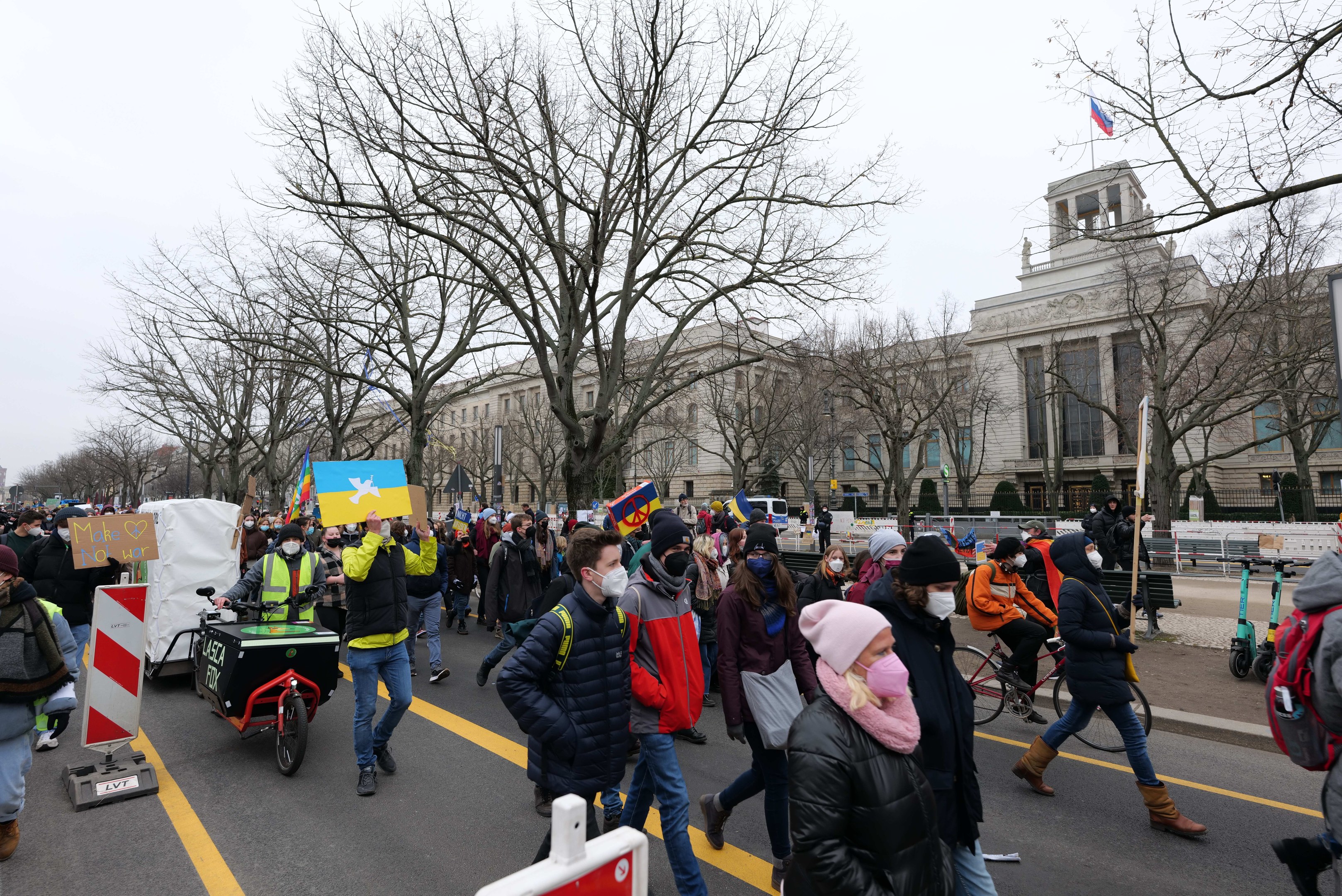 Eine große Protestdemo mit Menschen, die eine Straße in Washington, D.C. entlanggehen, einige halten Schilder und andere fahren Fahrräder, mit Bäumen, Schildern und einem klaren blauen Himmel im Hintergrund.