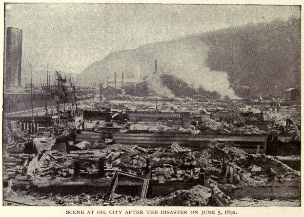 Schwarzes und weißes Foto einer Stadt nach einer Katastrophe am 5. Juni 1892, das Gebäude, Strommasten, Rauch und einen Hügel im Hintergrund zeigt, mit Text am unteren Rand.