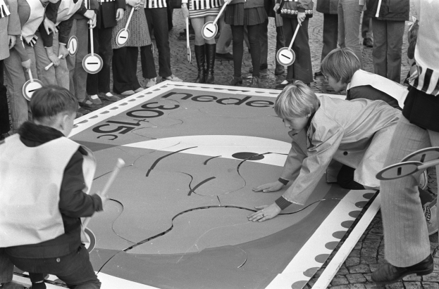 Schwarz-weißes Bild von Kindern, die Hopse spielen, einige halten Stöcke.
