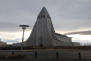 Ein Gebäude mit einer Uhr an der Fassade, umgeben von Bäumen, mit einem Strommast im Vordergrund.