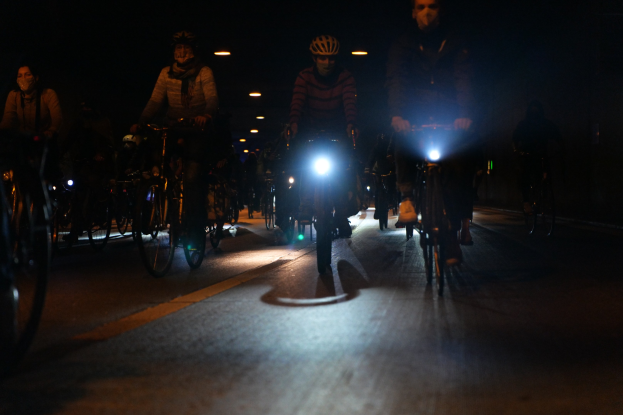 Radfahrer mit Helmen fahren nachts eine hell erleuchtete Stadtstraße entlang.