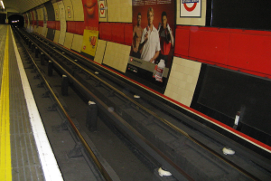 A train track with posters on the wall beside it.