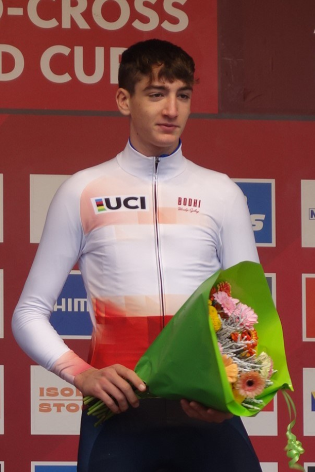 Ein Mann steht auf einem Podium und hält einen Blumenstrauß, feiernd mit einem selbstbewussten und stolzen Gesichtsausdruck.