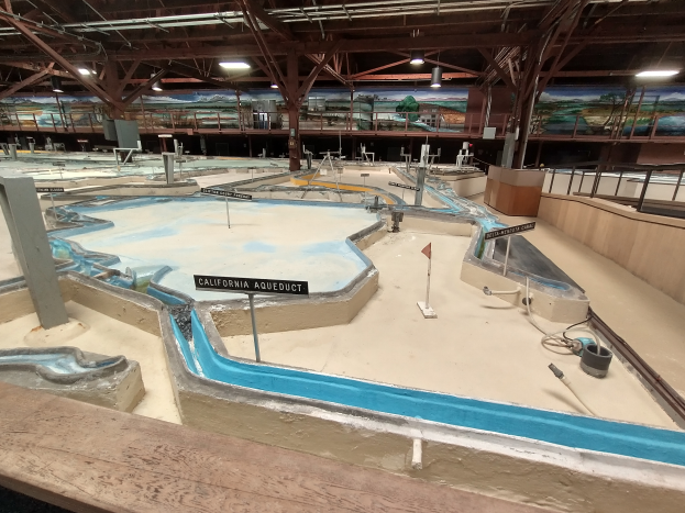 Ein großes Indoor-Wasserpark mit zahlreichen Wasserrutschen, Pfählen, Texttafeln, Deckenleuchten und Wandgemälde, das einem Minigolfplatz ähnelt.