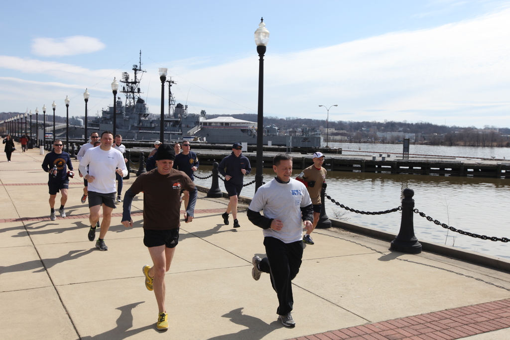 Eine volle Br√ľcke mit laufenden Menschen, Laternenpf√§hle, Wasser, Berge und Geb√§ude im Hintergrund.