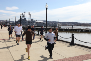 Eine volle Br√ľcke mit laufenden Menschen, Laternenpf√§hle, Wasser, Berge und Geb√§ude im Hintergrund.