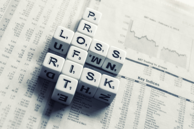 Kreuzworträtsel mit den Wörtern "Verlust", "Risiko" und "Risiko" auf einer Zeitung voller Finanztext und -zahlen.