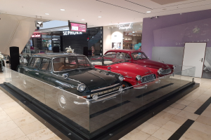 Eine Autohalle mit einer Glasvitrine voller Oldtimer, umgeben von Blumensträußen, Namensschildern, Deckenleuchten und anderen Gegenständen.