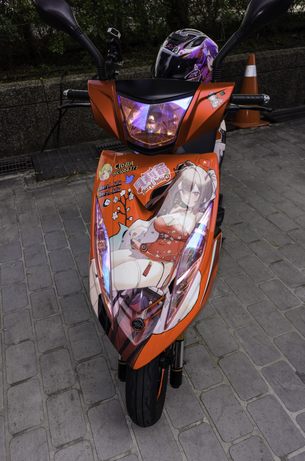 Ein oranger Roller, der auf einer Straße geparkt ist, mit einem Helm daneben, neben einem Verkehrskegel, einer Wand und Bäumen im Hintergrund.