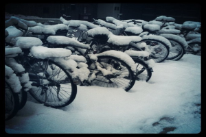 Mehrere Fahrräder stehen auf einem schneebedeckten Boden, wobei der Schnee auch die Fahrräder bedeckt.