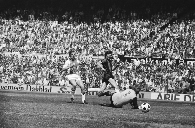 Schwarzes und weiße Foto von Männern, die auf einem Feld Füssball spielen, mit Zuschauern im Hintergrund und einem Banner "Bundesliga 1978-79 Ajax 1-1 Hannover 96".