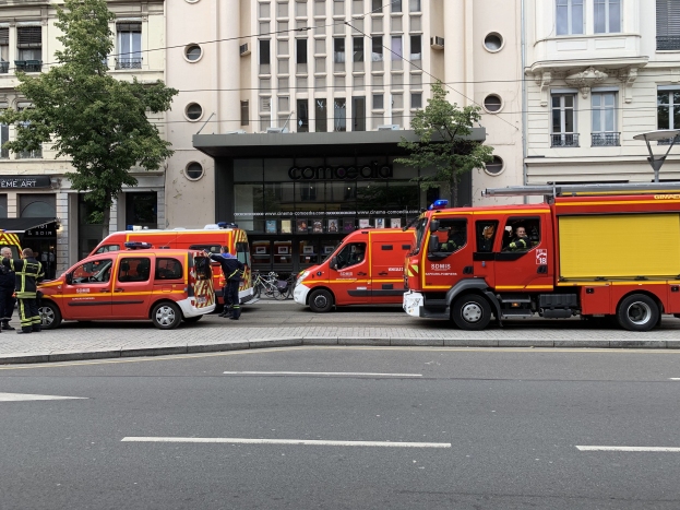 Feuerwehrfahrzeuge auf einer Straße in Paris geparkt mit Menschen in der Nähe, Gebäuden, Bäumen und einem Fahrrad im Hintergrund, wahrscheinlich an einem Unfallort.