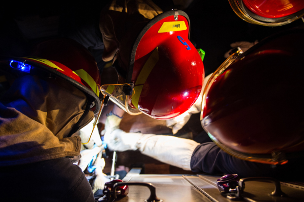 Feuerwehrleute mit Helmen und Handschuhen arbeiten an einem Feuerwehrauto in der Nacht mit Notfallversorgung auf einem Tisch rechts.